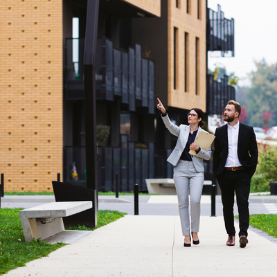 A man and a woman are walking down a sidewalk in front of a building.