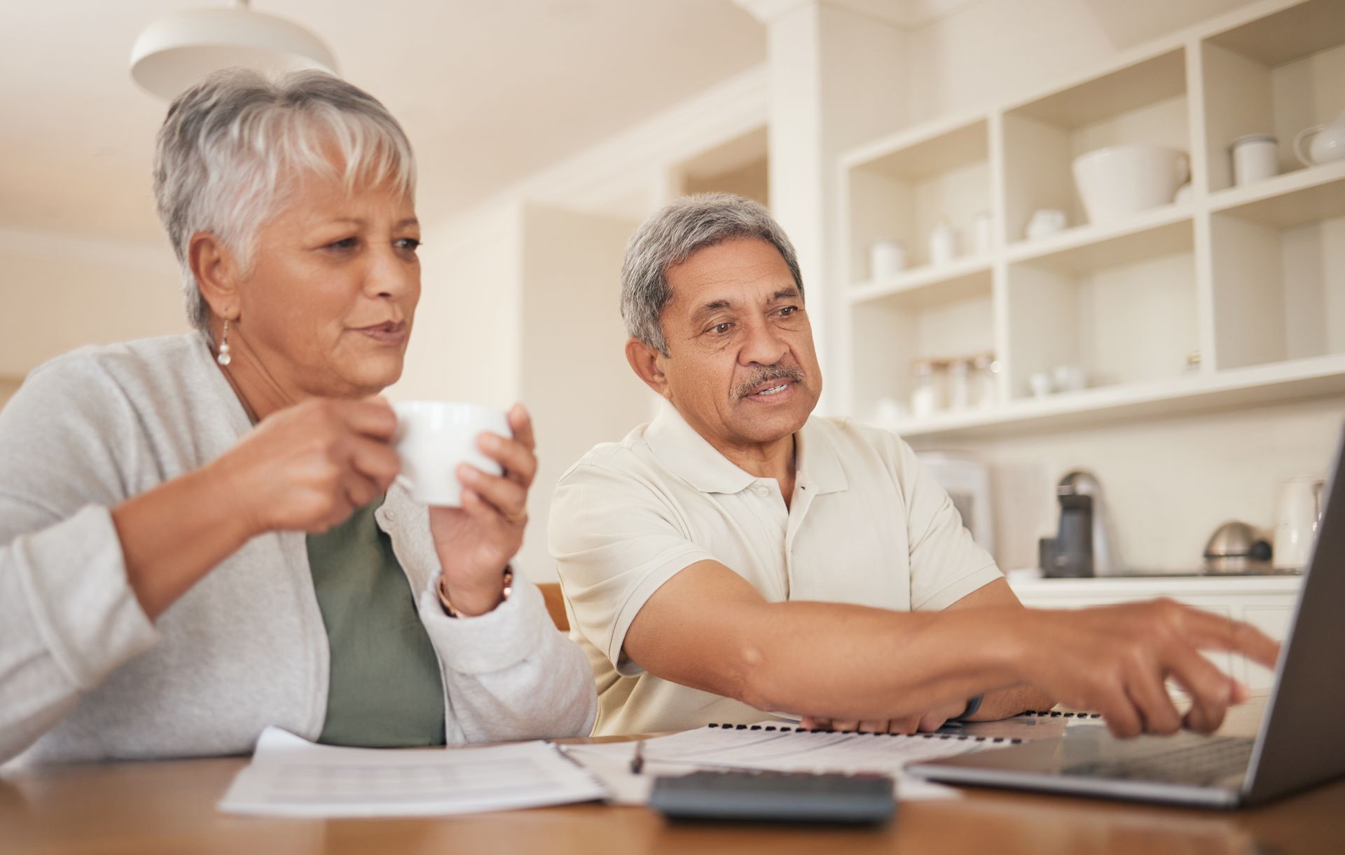An older couple is sitting at a table looking at a laptop computer.