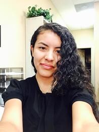 Agent Hayllens with curly hair is taking a selfie in a room.