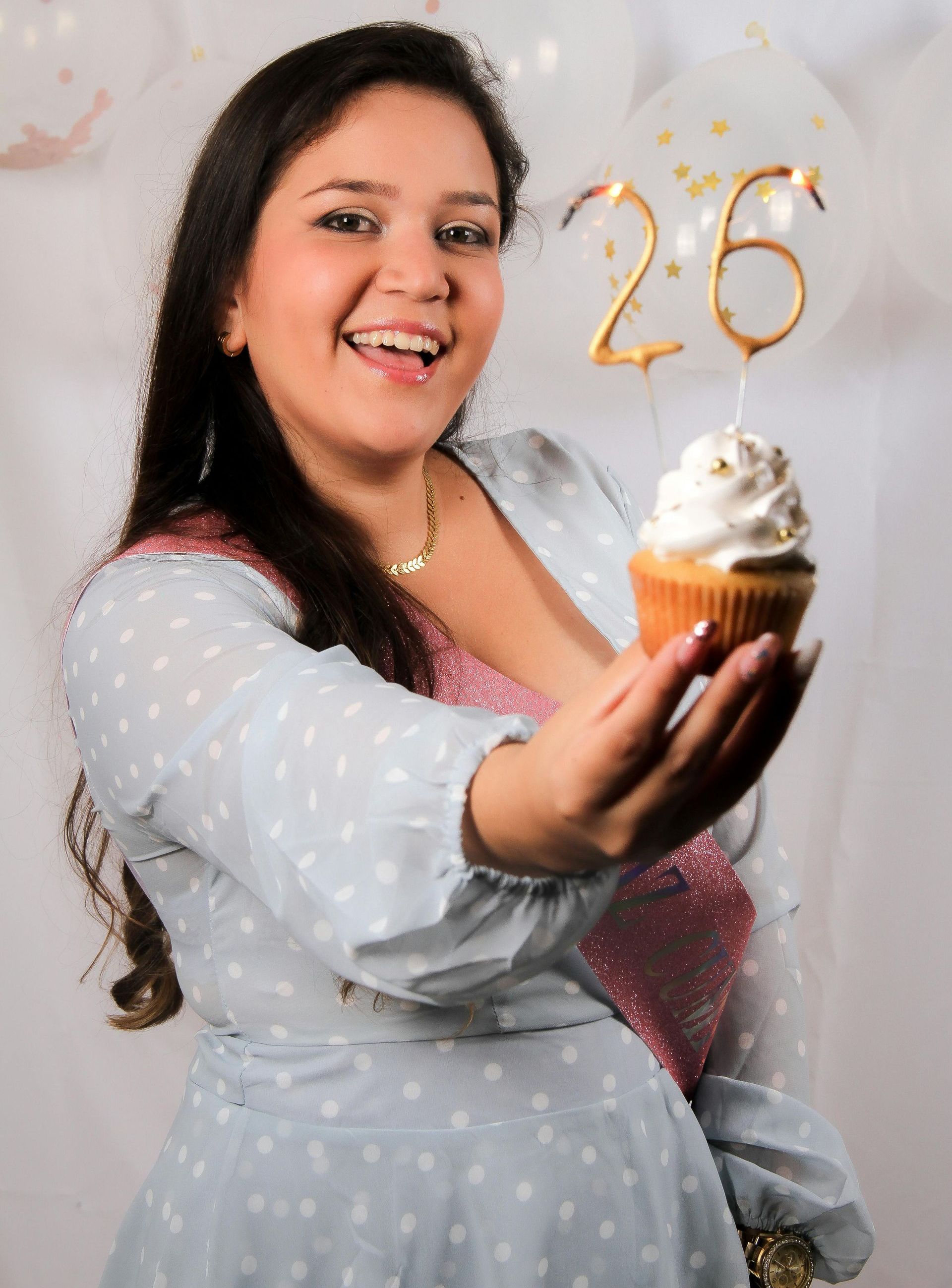 A woman is holding a cupcake with the number 26 on it