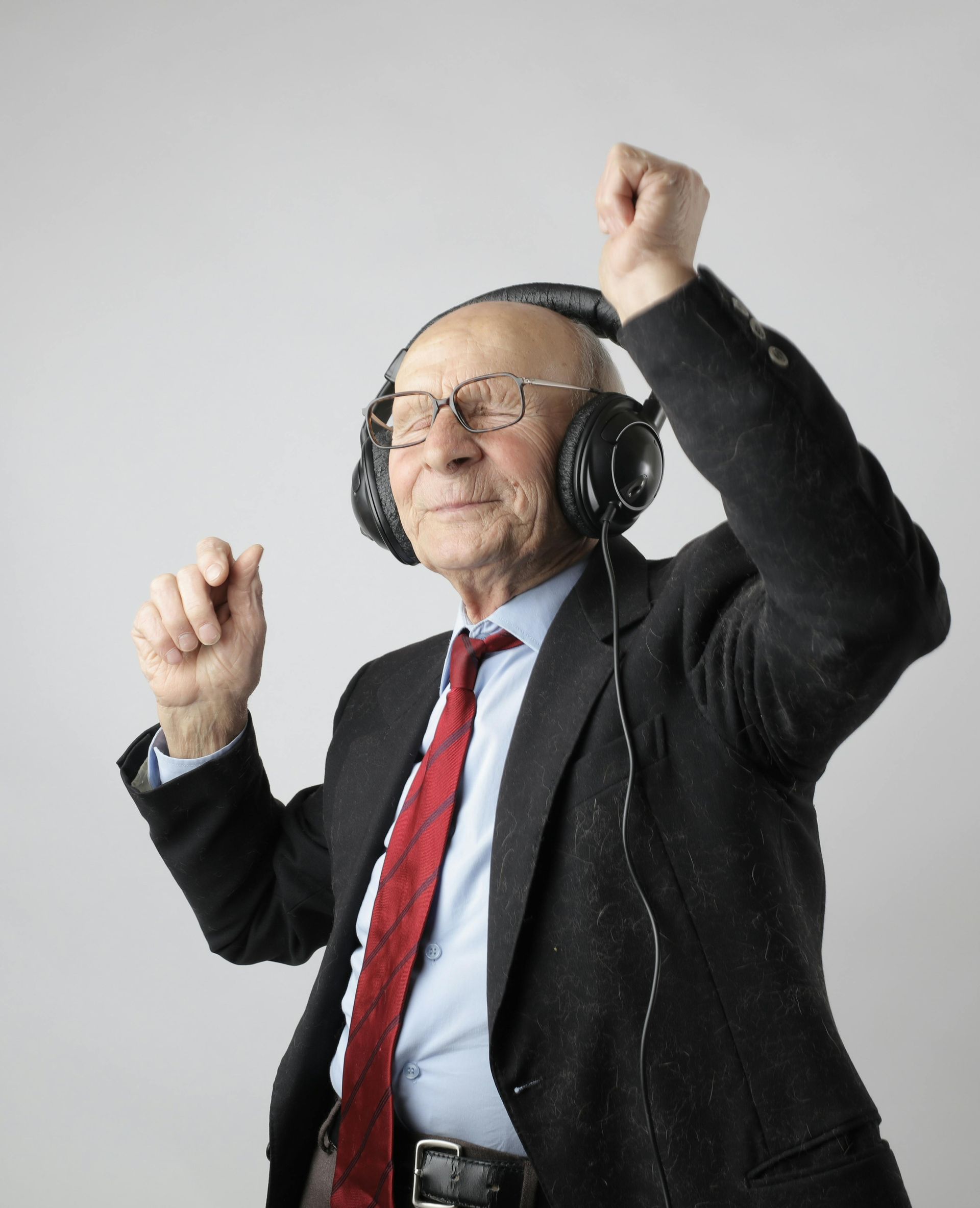 An elderly man in a suit and tie is wearing headphones and dancing.