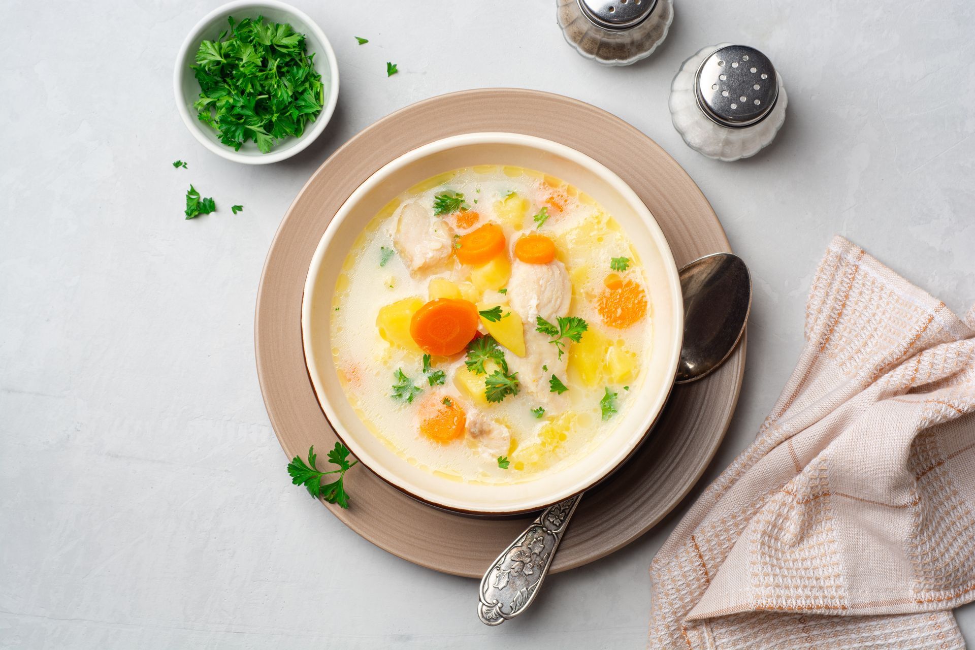 A bowl of chicken soup with carrots and potatoes on a plate with a spoon.