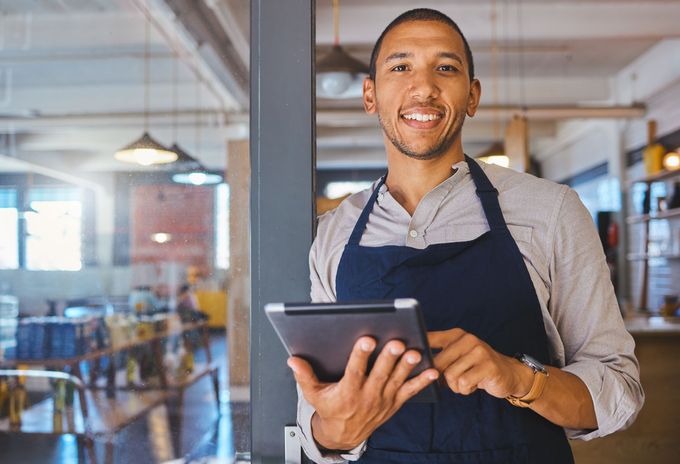 A man in an apron is holding a tablet in a restaurant.