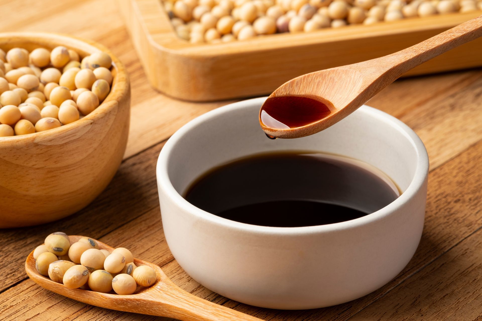 A wooden spoon is pouring soy sauce into a bowl.