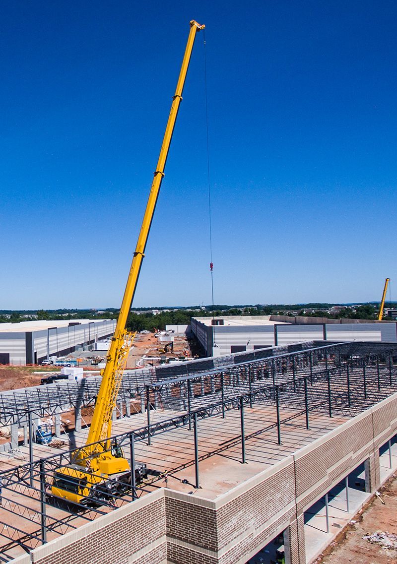 Yellow crane lifting materials at a construction site; blue sky in background.