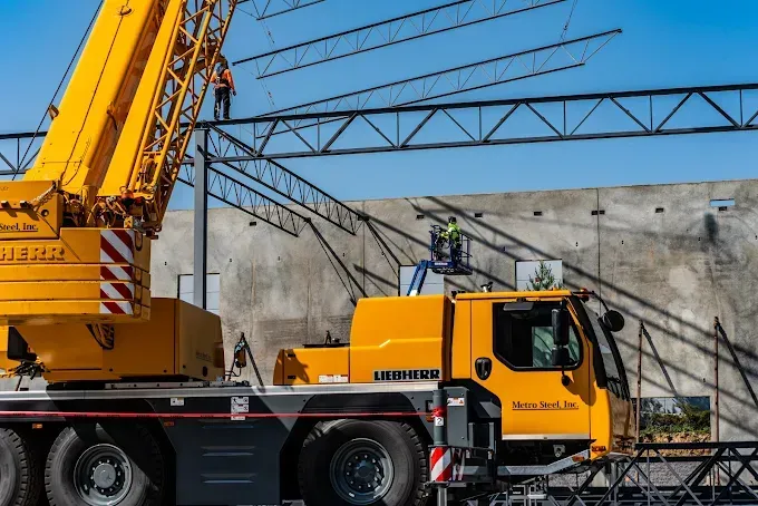 Yellow crane lifting steel beams during building construction. Workers on beams and in lift.