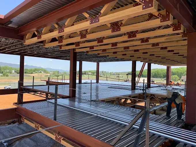 Construction site with steel framework and wooden beams, worker on a corrugated metal deck, outdoor setting.
