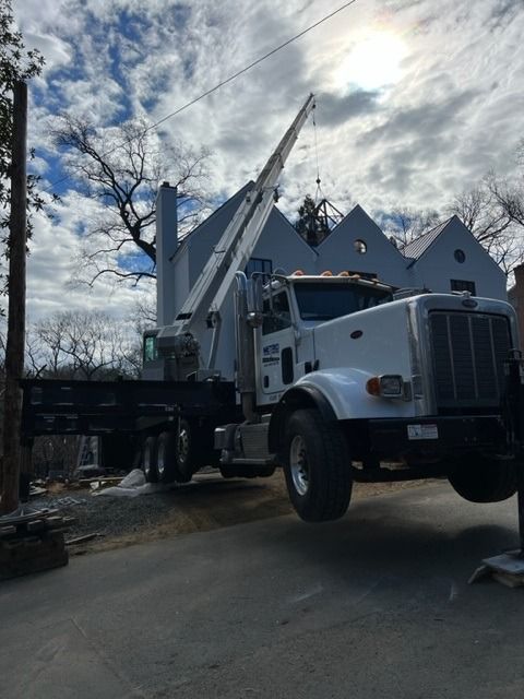 A large crane lifting a house gable; white truck, overcast sky, construction site.