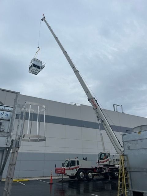 Crane lifting a metal unit near a building. Rainy day.