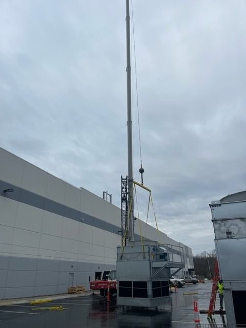 Crane lifting an industrial cooling tower near a large building on a cloudy day.