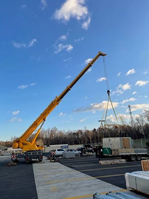 Yellow crane lifting a large object from a flatbed truck against a blue sky.