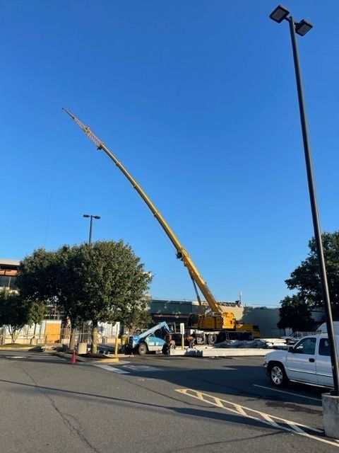 A large crane with an extended boom is working near a building on a sunny day.