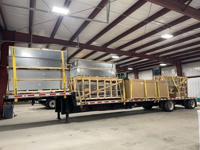 Two flatbed trailers loaded with crates and metal panels inside a warehouse.