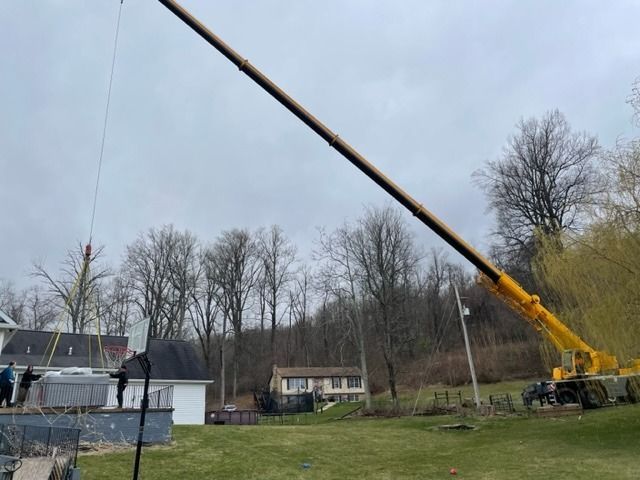 Yellow crane lifting a large rectangular object near a house on a cloudy day.