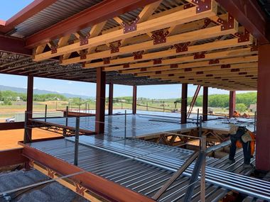 Steel-framed building under construction. Workers on corrugated metal decking, with exposed beams and trusses.