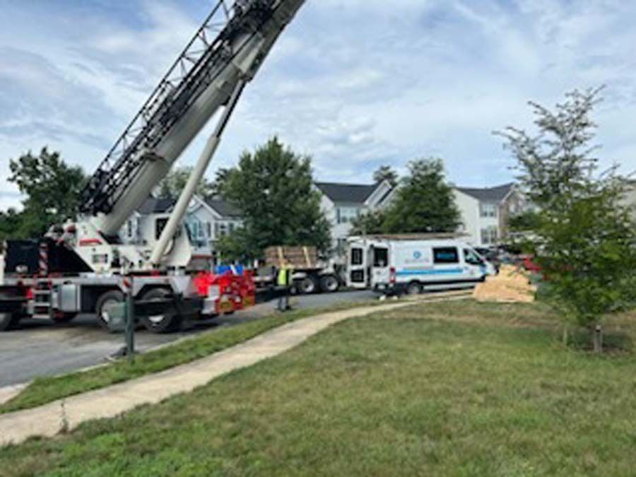Crane lifting materials near a residential area with parked vans and houses in the background.