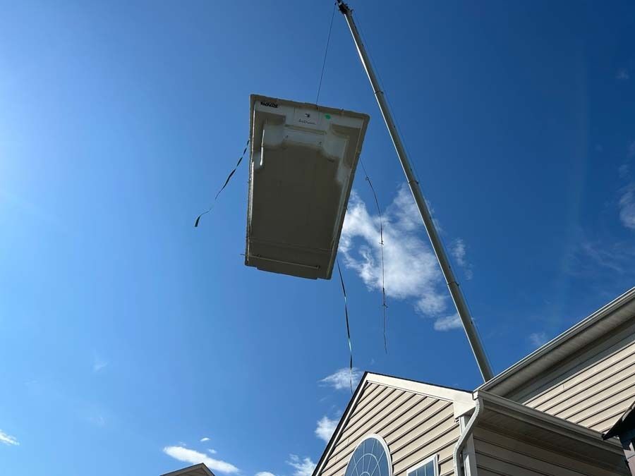 A bathtub suspended in the air by a crane, above a house with a blue sky.
