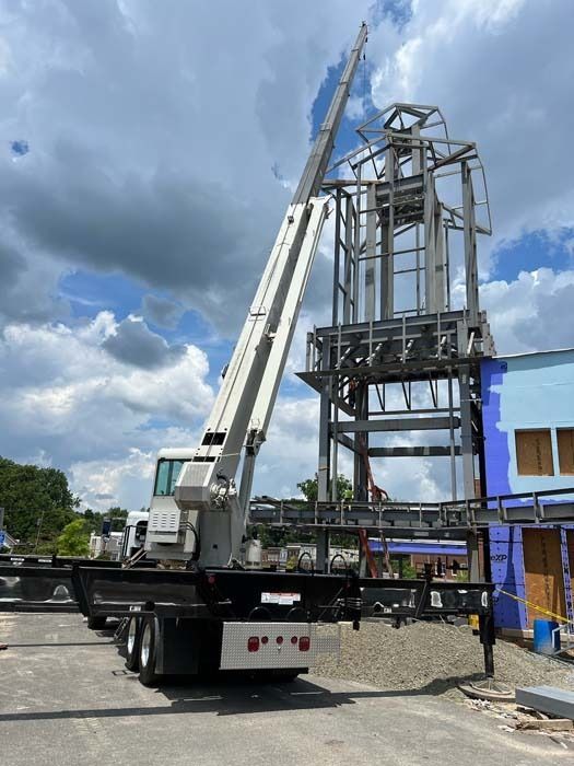 A crane lifting a metal frame structure next to a building on a partly cloudy day.