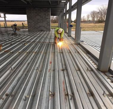 Construction worker welding metal decking on a building frame, sparks flying. Outdoors.