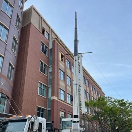 Crane next to a brick building. The crane is tall and white. Blue sky.