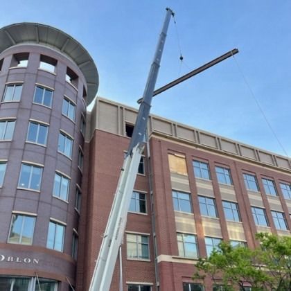 Crane lifting a beam onto a brick building with a rounded tower. Blue sky.