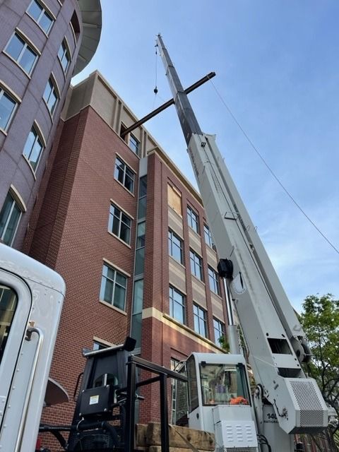 A crane lifting a beam towards a brick and beige building.