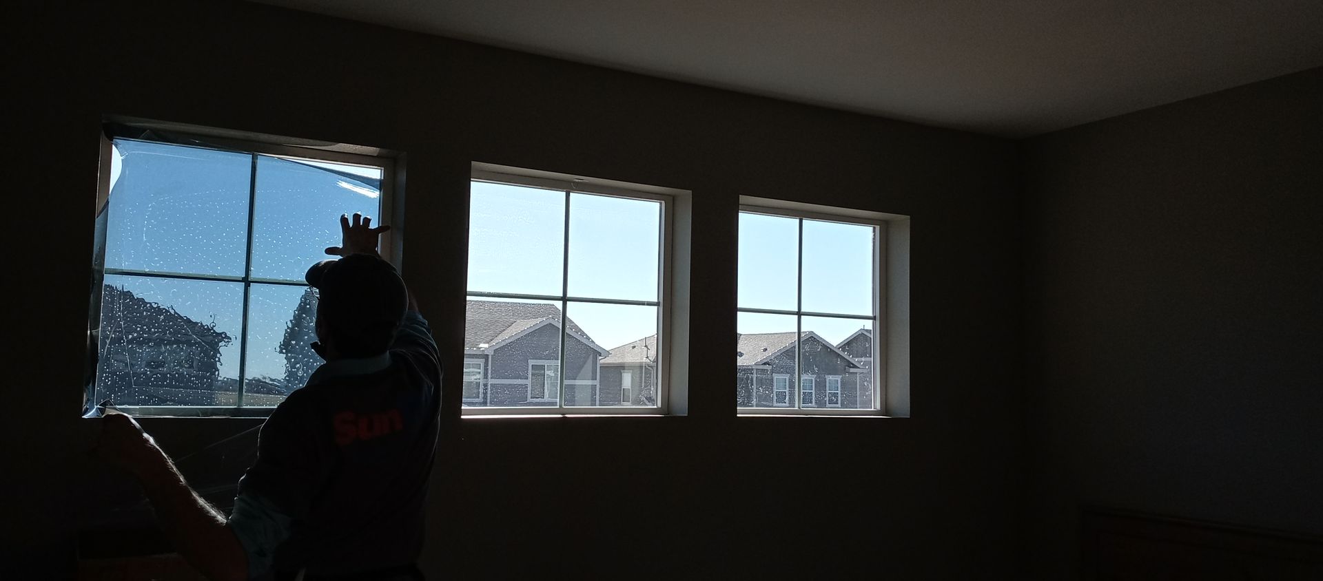 A man is standing in an empty room installing window tint