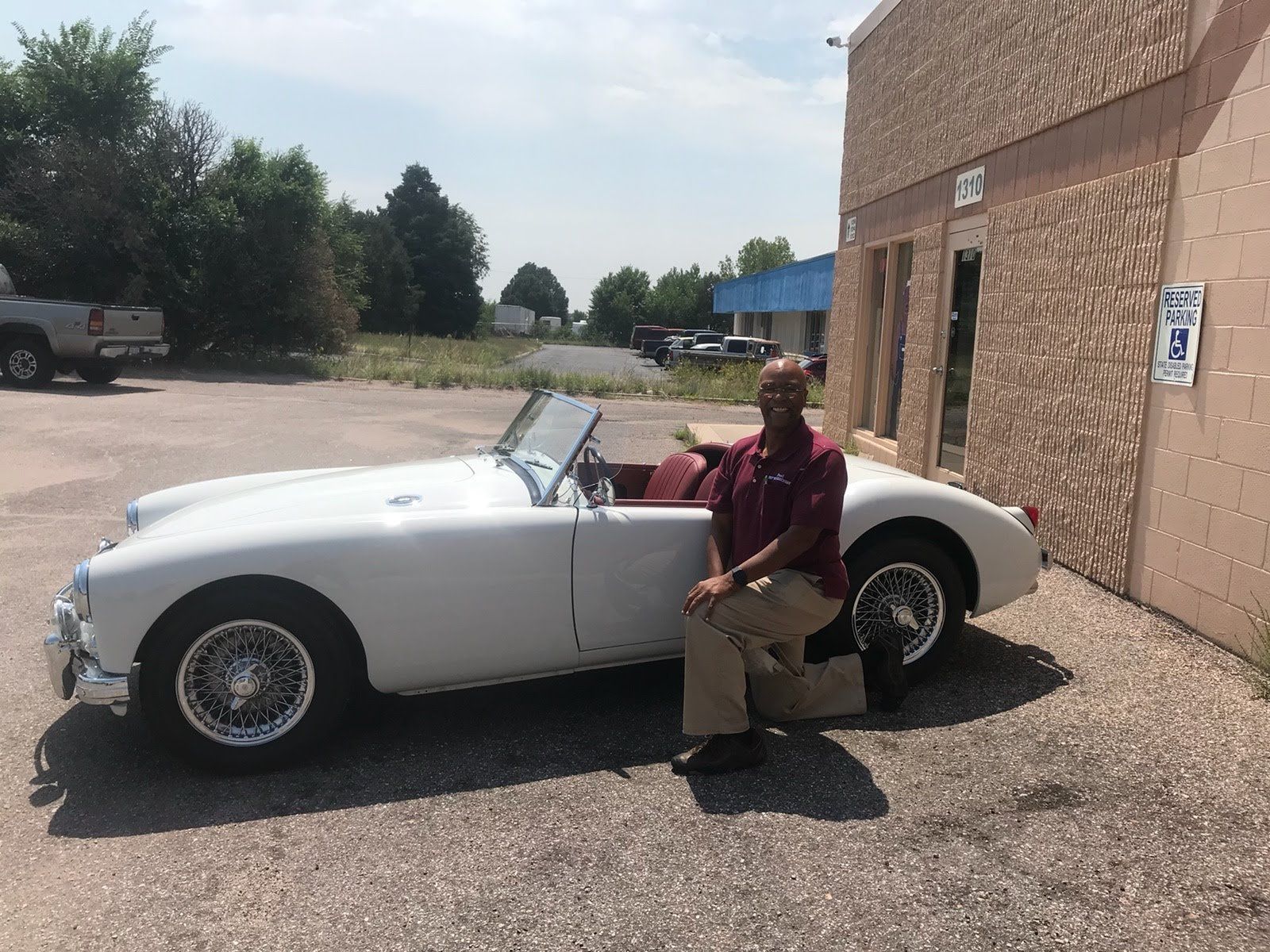 Paul Hasty is sitting next to a white sports car in a parking lot.