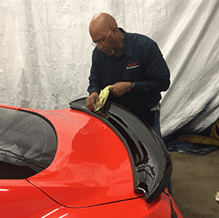 Paul Hasty is polishing the rear wing of a red car.