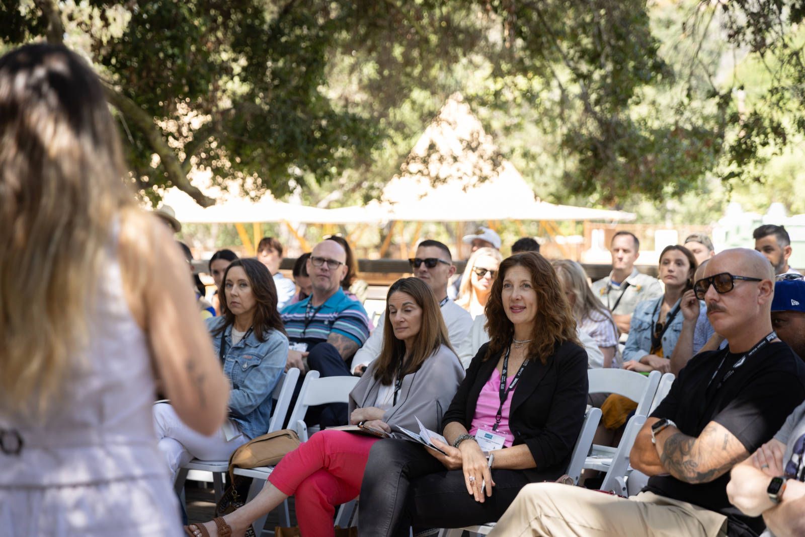 A woman is standing in front of a crowd of people sitting in white chairs.