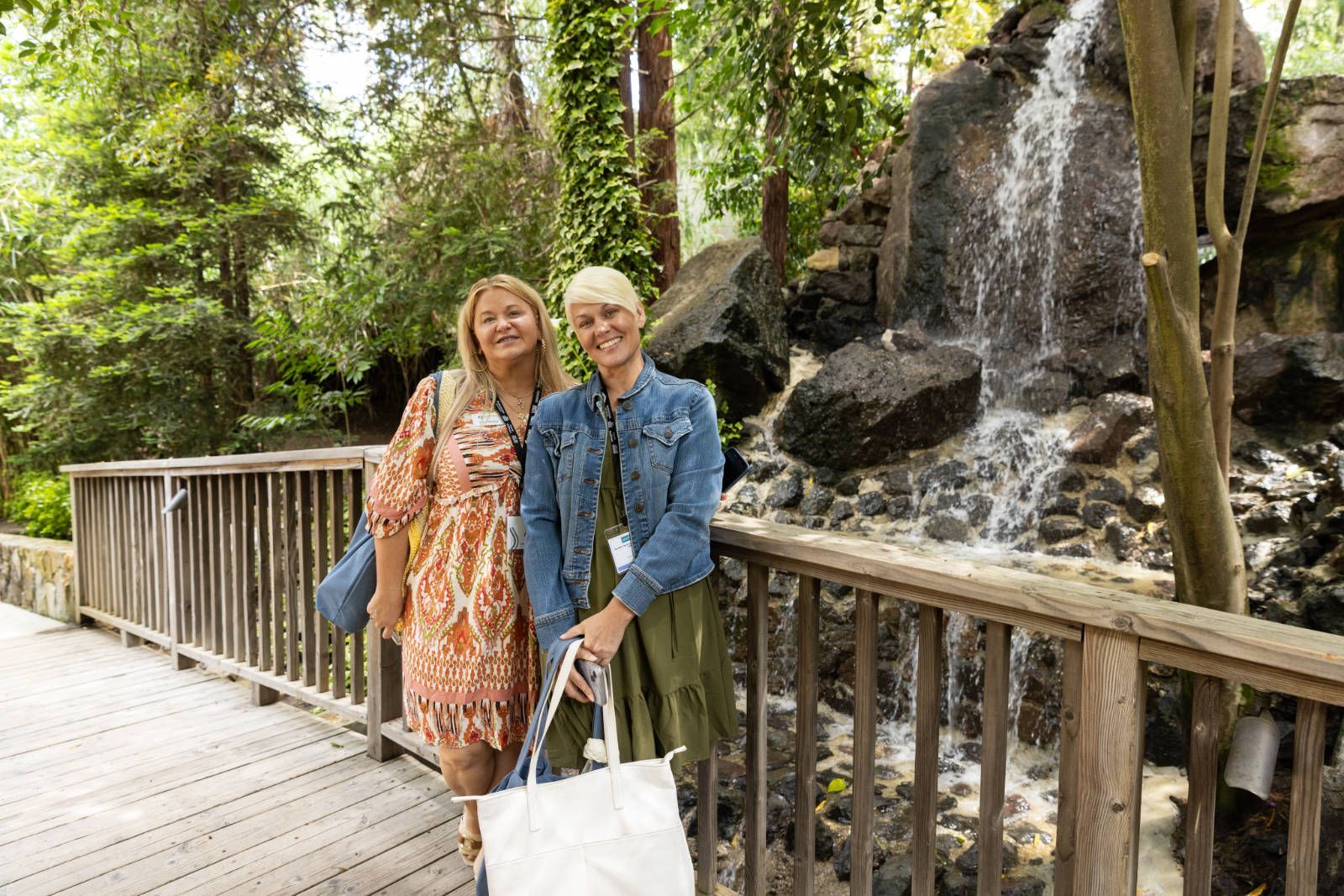 Two women are standing on a bridge in front of a waterfall.