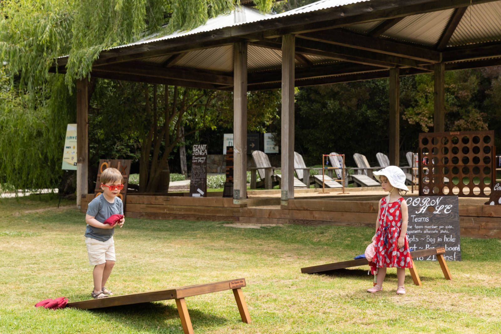 A boy and a girl are playing a game of cornhole in a park.
