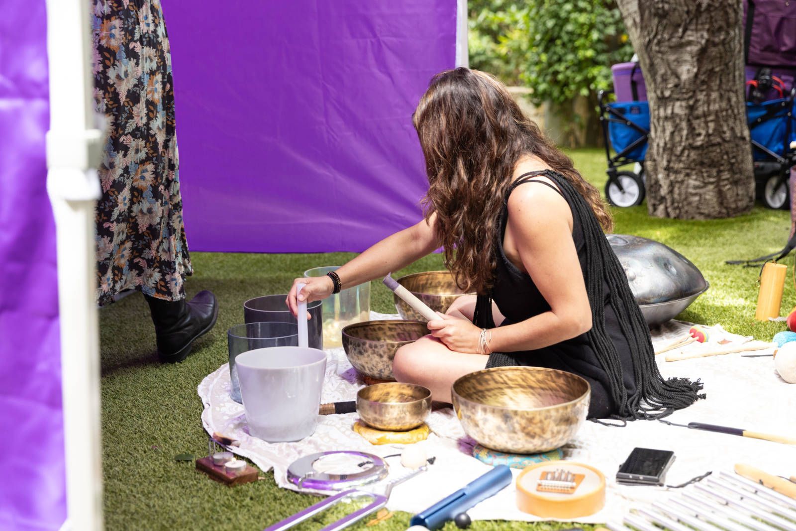 A woman is sitting on the grass playing a sound bowl.