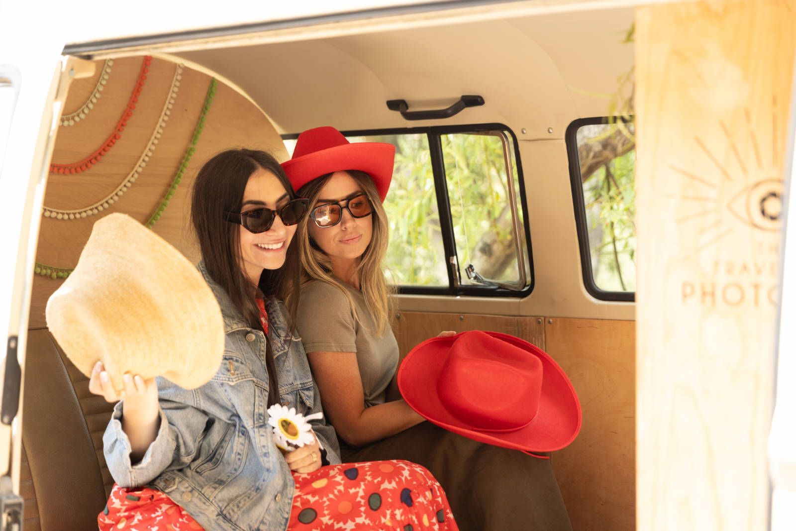 Two women are sitting in a van holding hats.