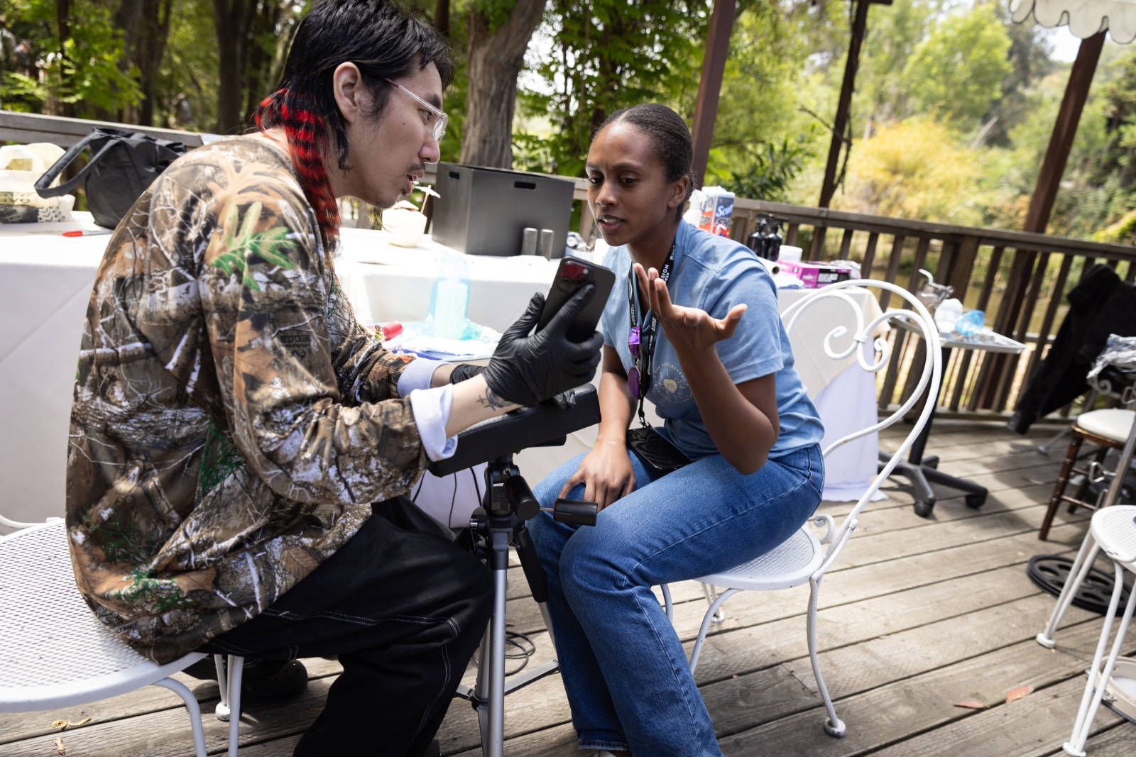 A man is kneeling down next to a woman sitting on a chair on a deck.
