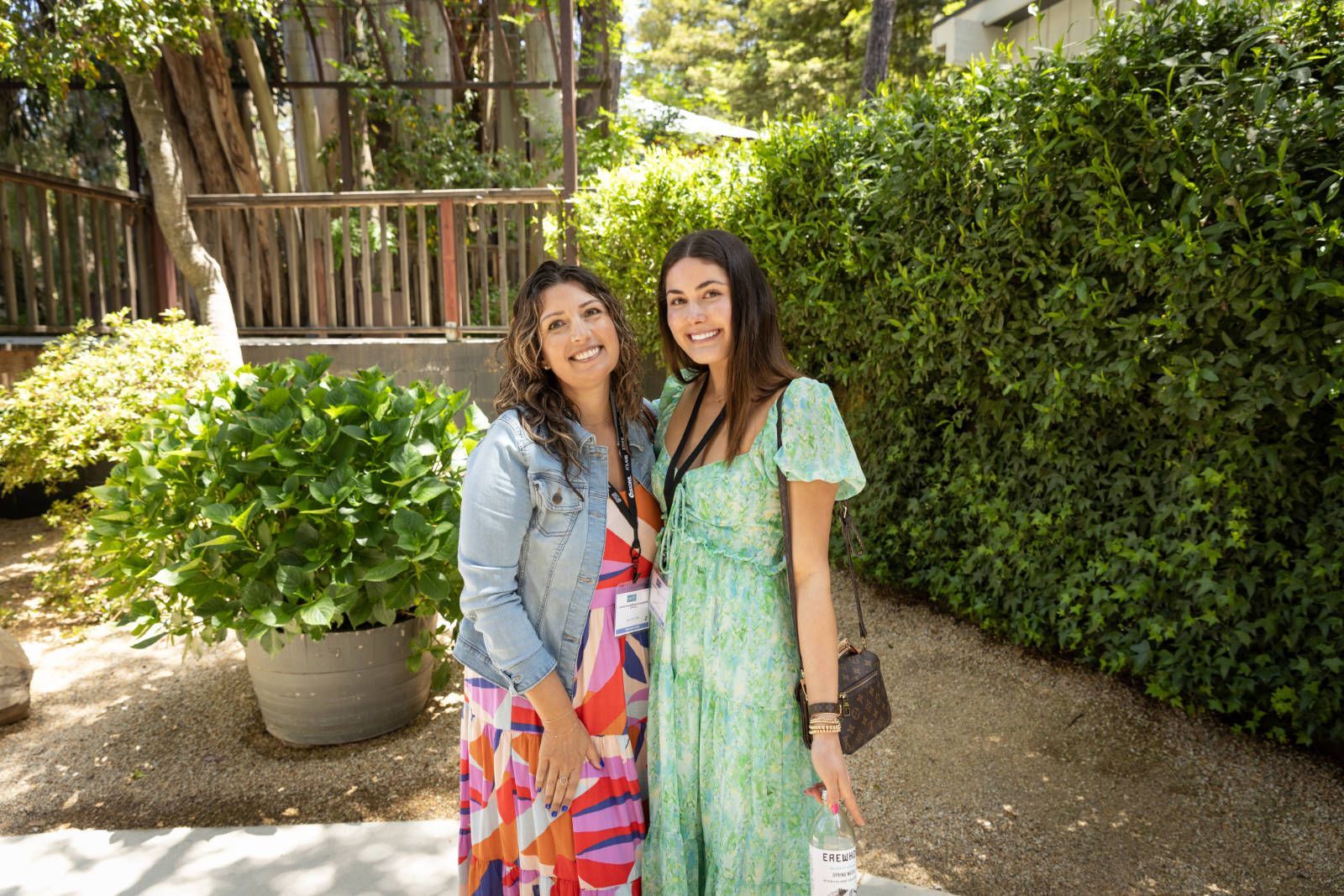 Two women are posing for a picture in front of a bush.