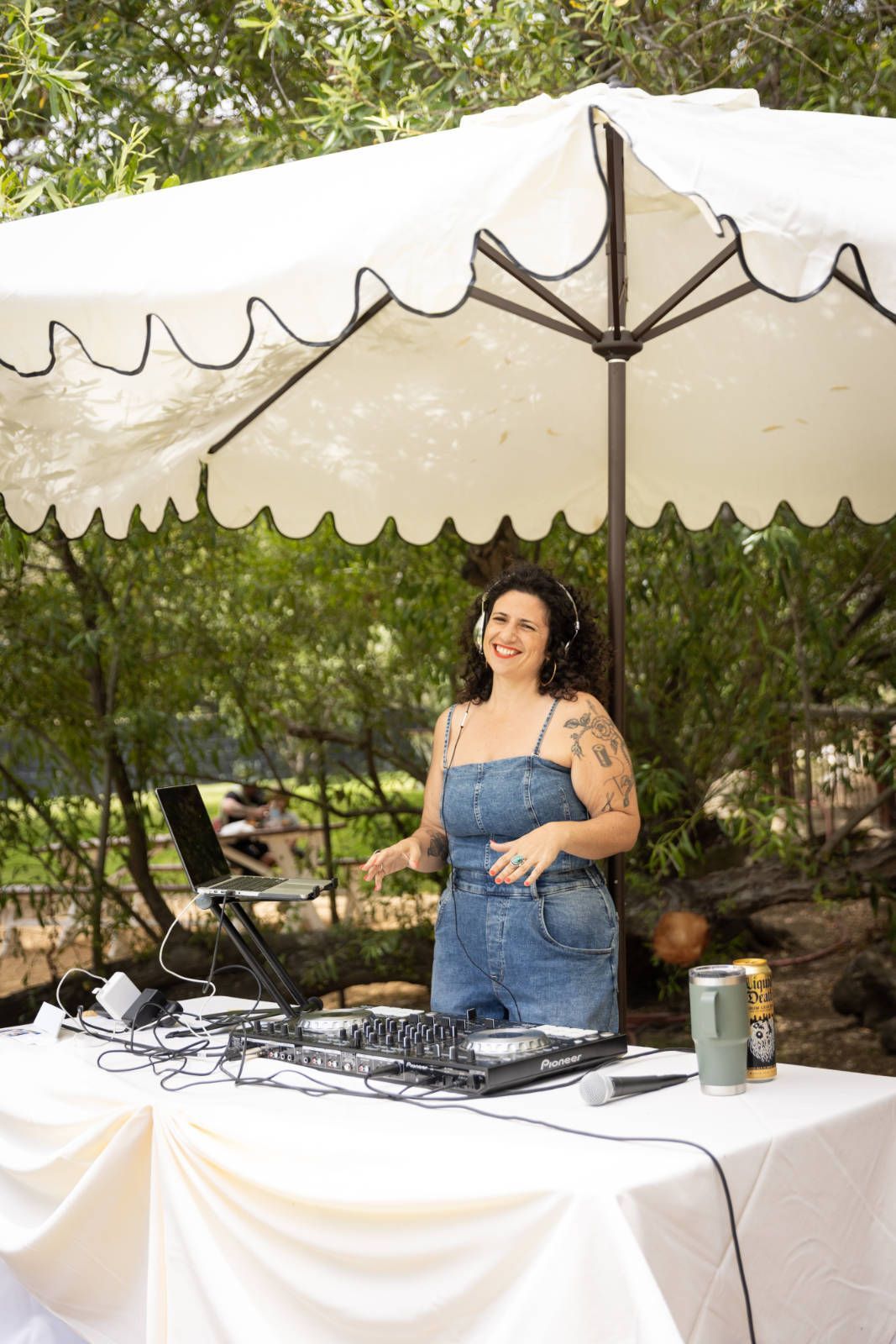 A woman is standing in front of a dj booth under an umbrella.