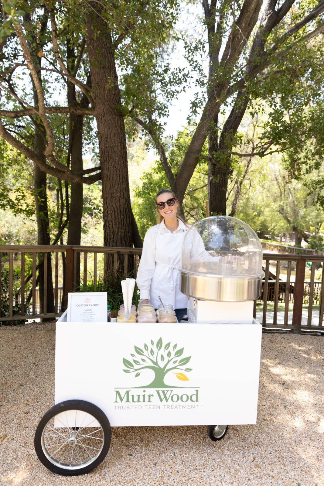 A woman is standing next to a cart filled with cotton candy.