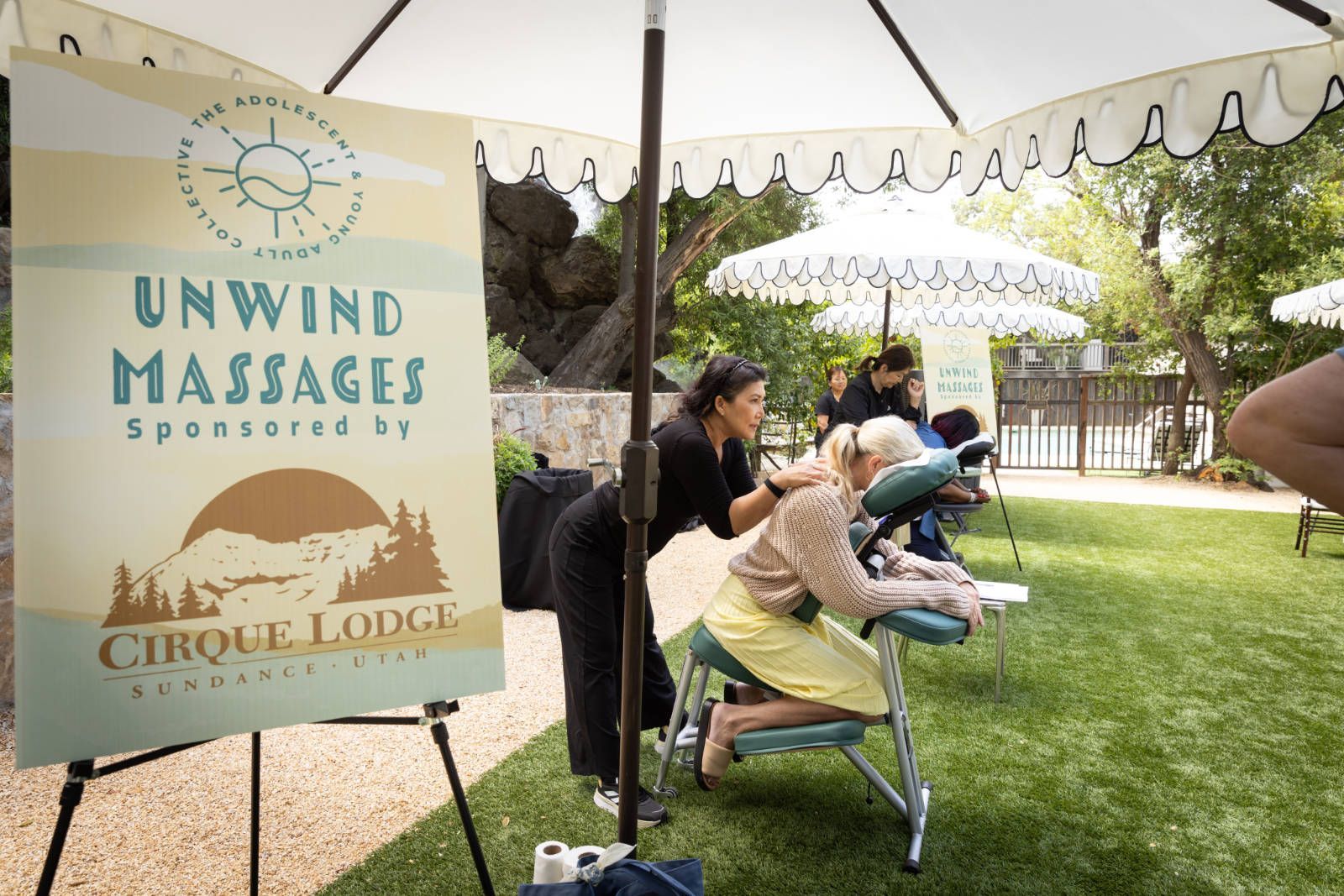 A woman is getting a massage under an umbrella sponsored by cirque lodge.