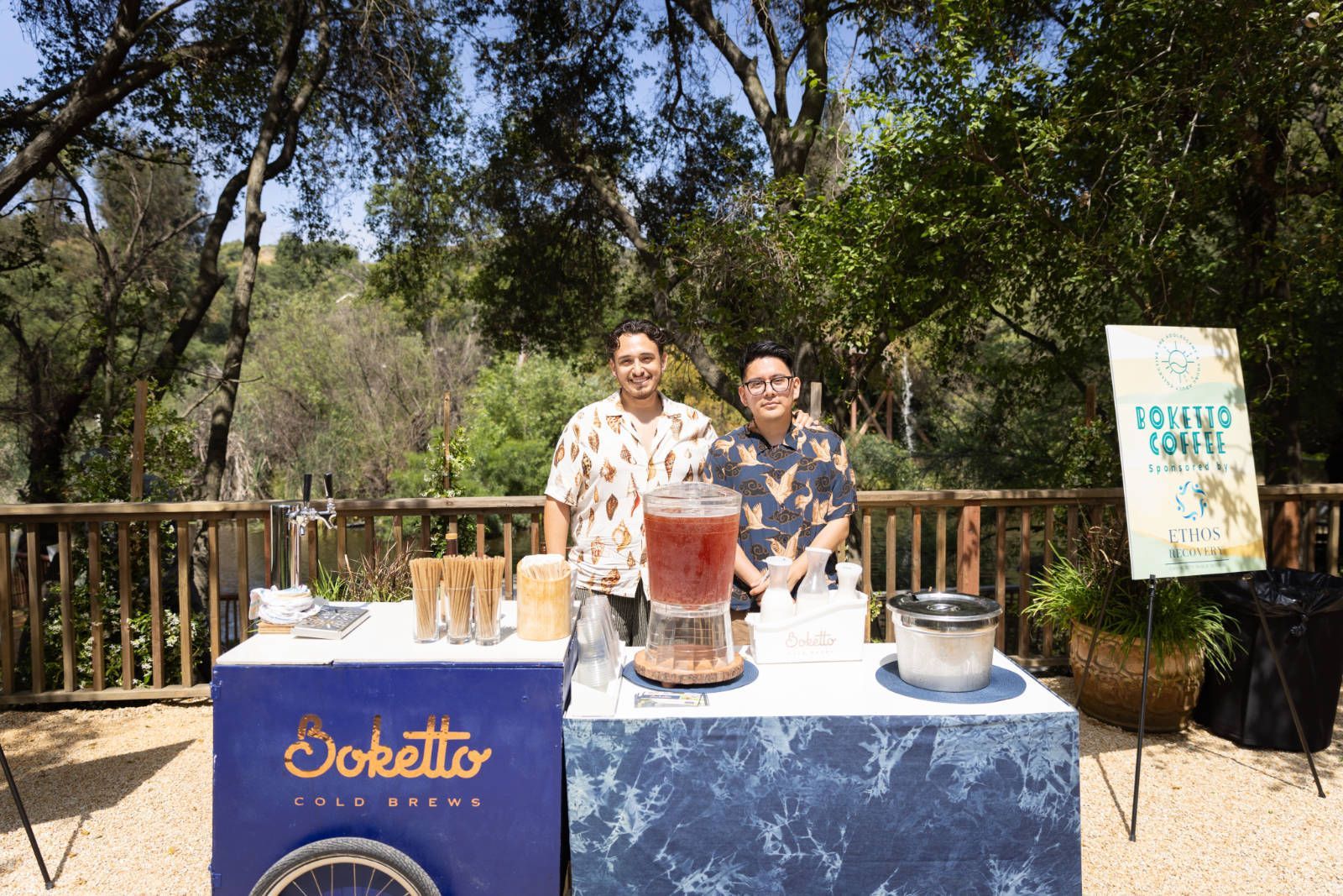 Two men are standing behind a table with a drink dispenser.