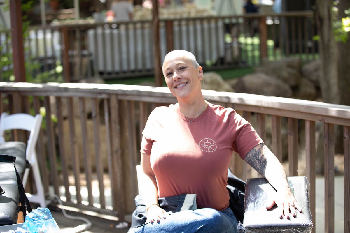 A woman with a shaved head is sitting on a bench on a deck.