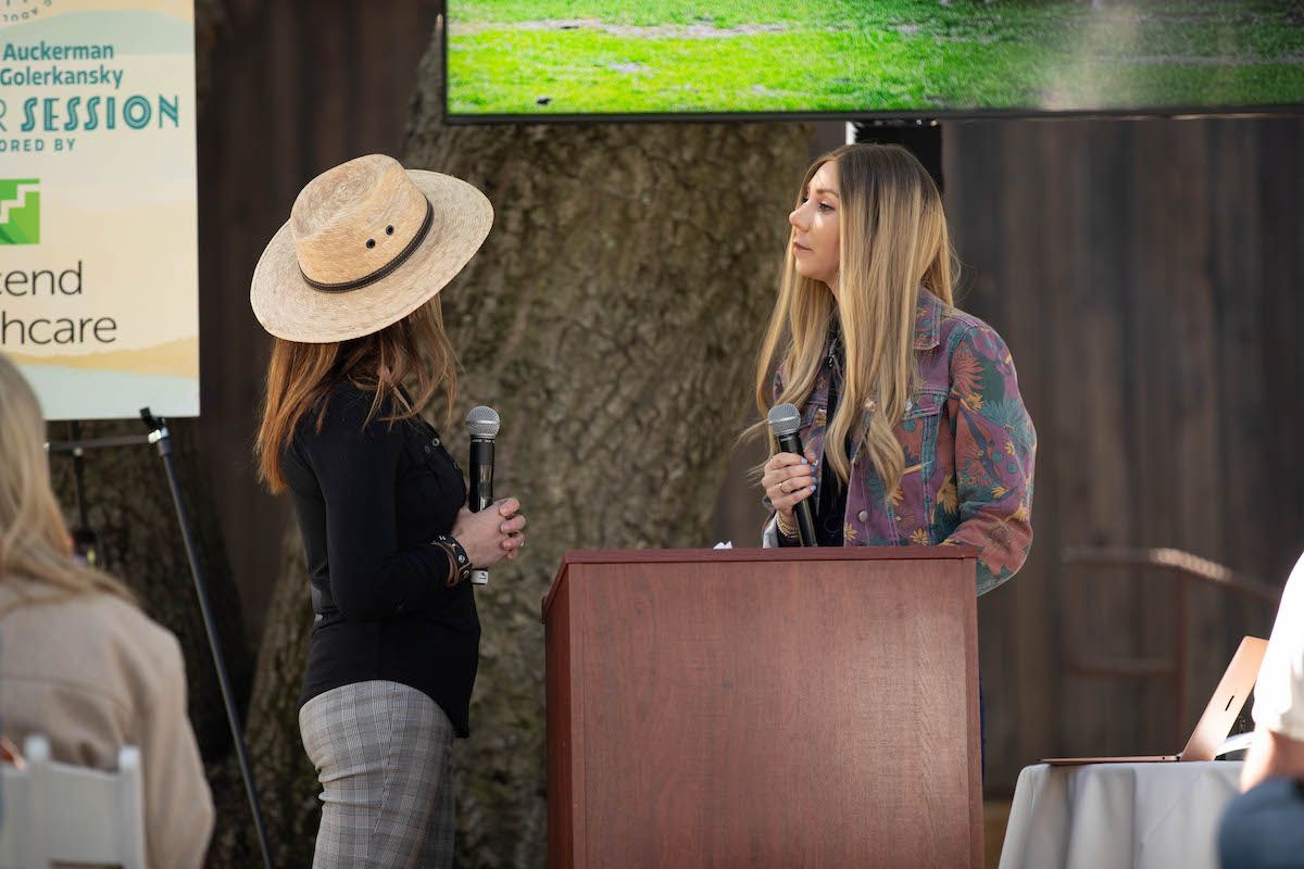 Two women are standing at a podium talking into microphones.
