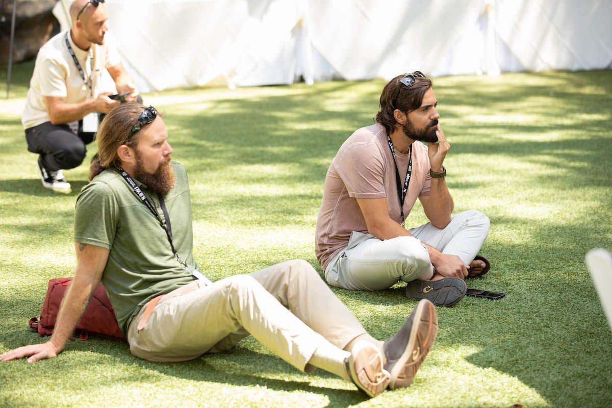 Two men are sitting on the grass with their legs crossed.