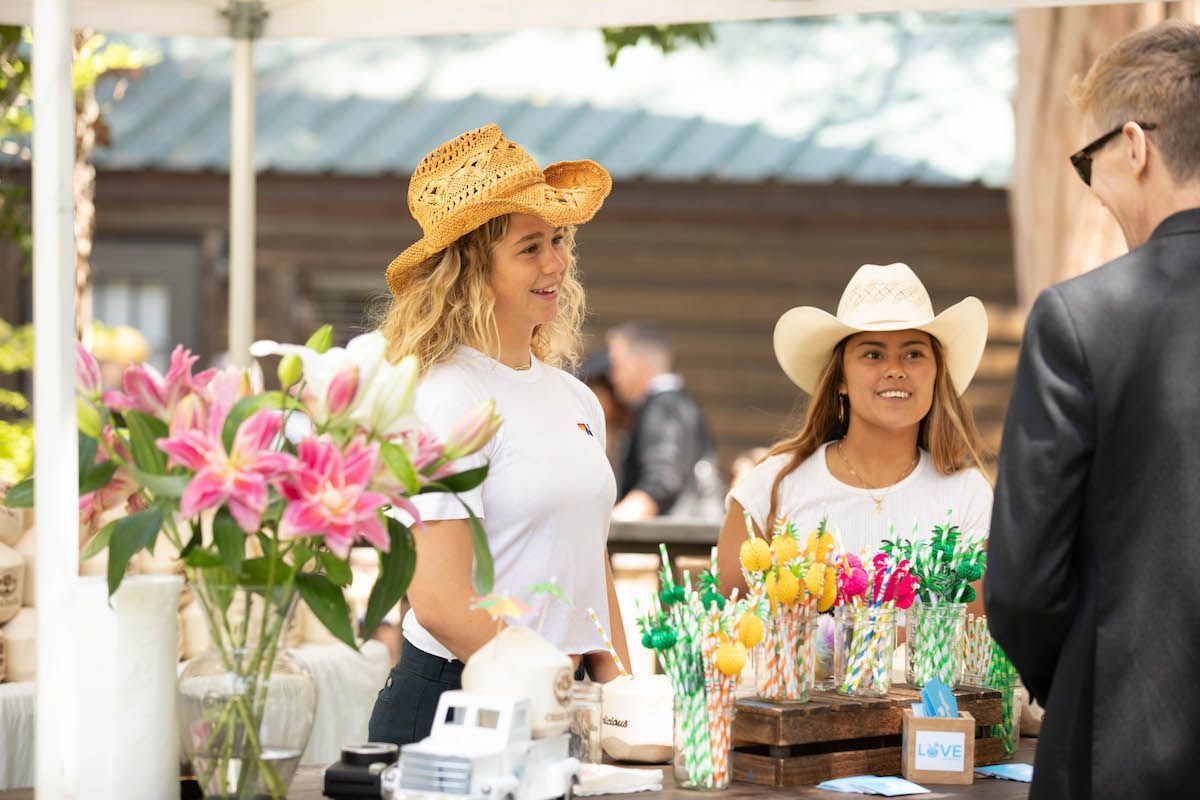 Two women wearing cowboy hats are talking to a man in a suit.