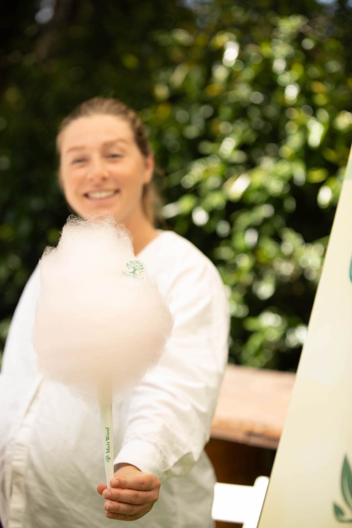 A woman in a white shirt is holding a stick of cotton candy.