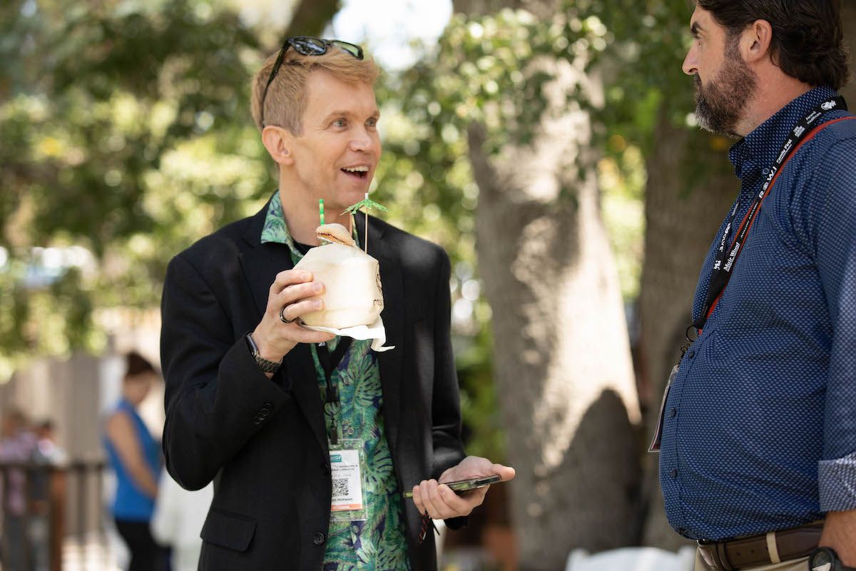 A man in a suit is holding a cup of coffee and talking to another man.