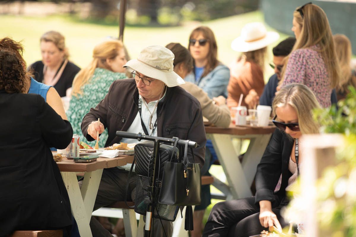 A group of people are sitting at picnic tables eating food.