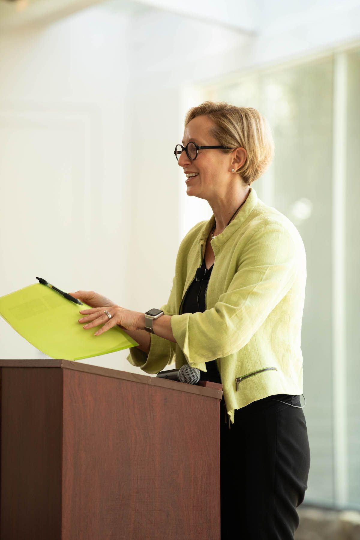 A woman is standing at a podium holding a yellow folder.