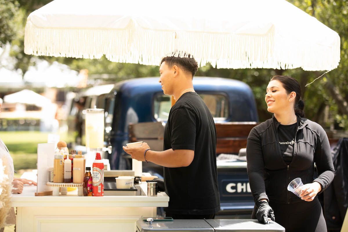 A man and a woman are standing in front of a food truck.
