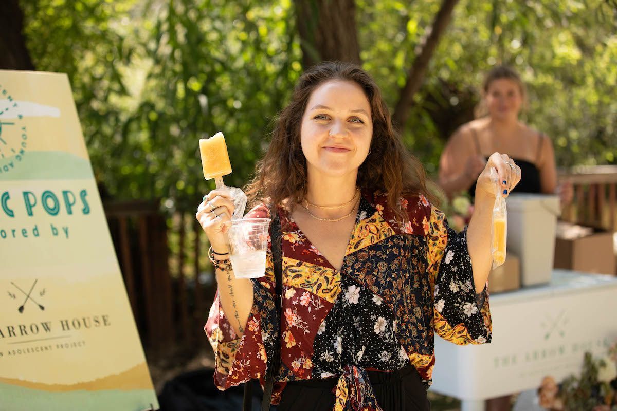 A woman is holding a popsicle in her hand in front of a sign.